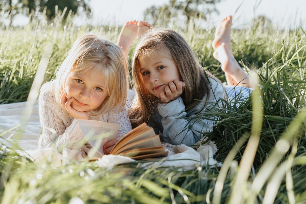 Two young girls enjoying a book on a blanket in a sunny grassy field. Perfect childhood moment.